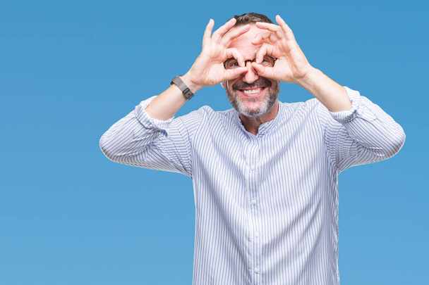 Middle age hoary senior man wearing glasses over isolated background doing ok gesture like binoculars sticking tongue out, eyes looking through fingers. Crazy expression. - Photo, Image