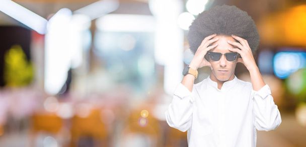 Молодий афроамериканець людиною з афро волосся носити сонцезахисні окуляри, які страждають від головного болю, відчайдушні і підкреслив, тому що біль і мігрень. Руки на голову. - Фото, зображення