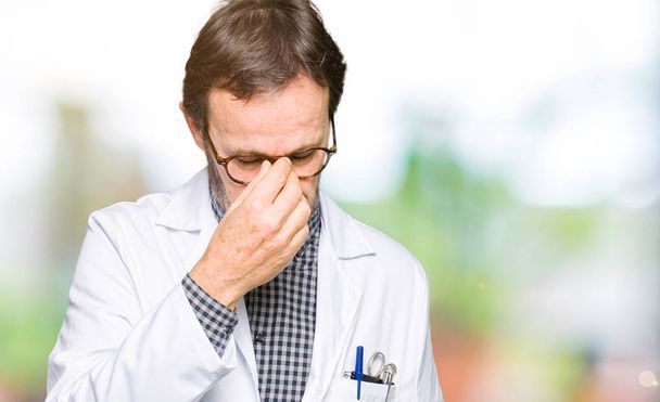 Middle age doctor men wearing medical coat tired rubbing nose and eyes feeling fatigue and headache. Stress and frustration concept. - 写真・画像