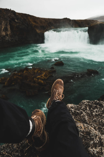 Hiker boots on rocks of cliff over waterfall in beautiful landscape in Iceland, Europe - Foto, Imagen