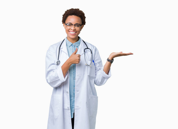 Nuori afrikkalainen amerikkalainen lääkäri nainen yllään lääketieteellinen takki yli eristetty tausta Näyttää kämmen ja tekee ok ele peukalot pystyssä, hymyillen onnellinen ja iloinen
 - Valokuva, kuva