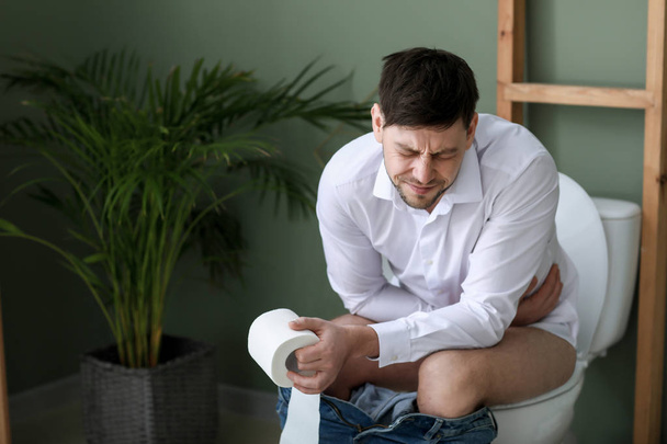Ο άνθρωπος που υποφέρει από διάρροια, ενώ κάθεται στην λεκάνη της τουαλέτας στο σπίτι - Φωτογραφία, εικόνα