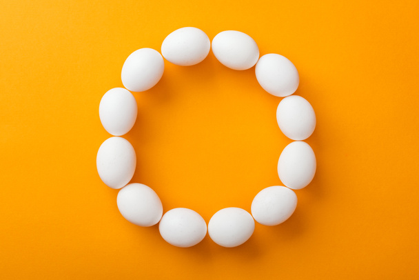 top view of whole white organic chicken eggs arranged in round frame on bright orange background with copy space - Foto, Imagen
