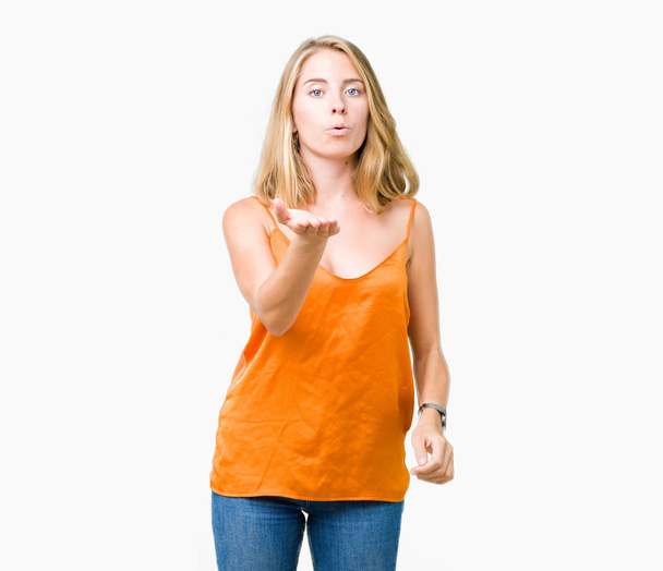 schöne junge Frau, die orangefarbenes Hemd über isoliertem Hintergrund trägt und in die Kamera schaut, die einen Kuss mit der Hand auf die Luft pustet, ist schön und sexy. Liebesausdruck. - Foto, Bild