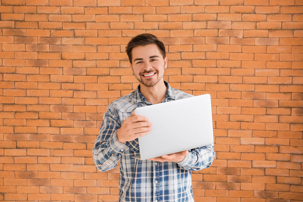 Mannelijke programmeur met laptop op baksteen achtergrond - Foto, afbeelding