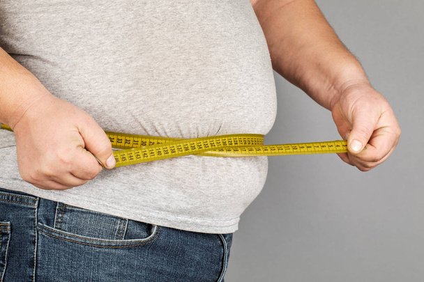Un homme mesure son gros ventre avec un ruban à mesurer. sur une ba grise
 - Photo, image