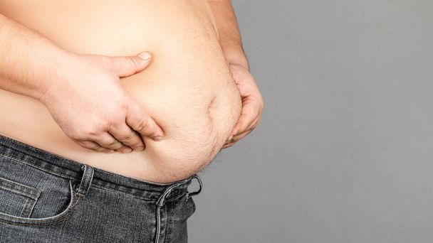 dikke man, het controleren van zijn gewicht, op een grijze achtergrond - Foto, afbeelding