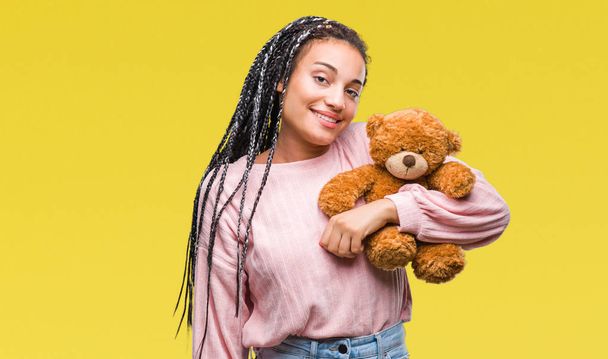 Young african american girl holding teddy bear over isolated background with a happy face standing and smiling with a confident smile showing teeth - Photo, image