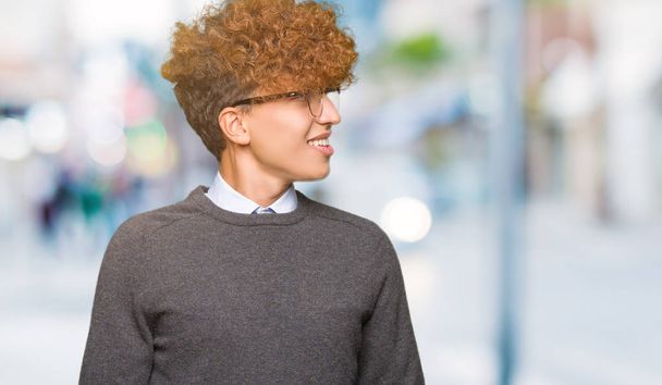 Young handsome business man with afro hair wearing glasses looking away to side with smile on face, natural expression. Laughing confident. - Photo, Image