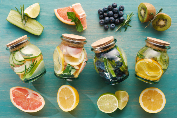 top view of detox drinks in jars with fruit ingredients on wooden surface - Фото, изображение