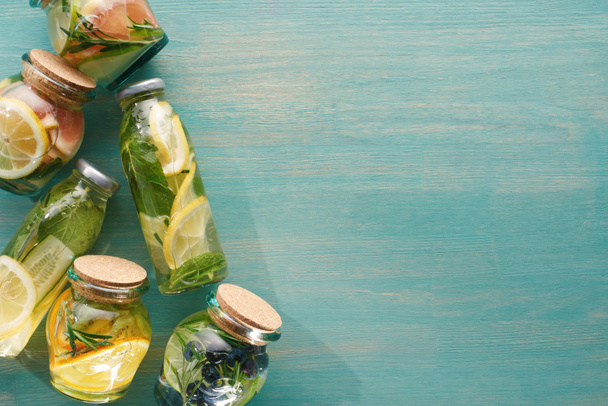 bovenaanzicht van detox verse dranken in flessen en potten met fruit, groenten, kruiden, bessen en groen - Foto, afbeelding