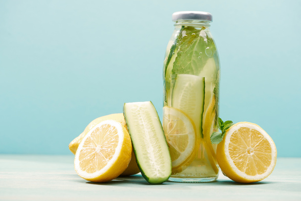 detox drink in bottle near lemons, mint and cucumber isolated on blue - Foto, Imagem