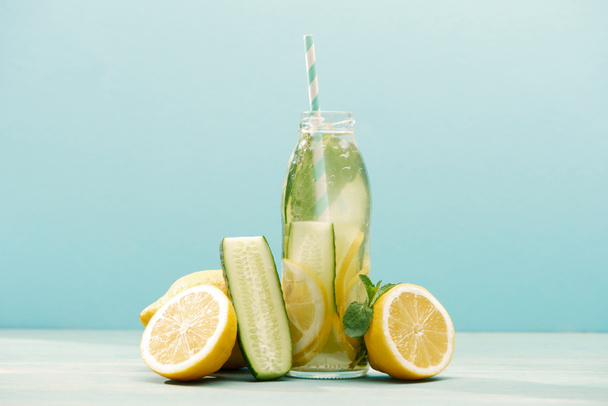detox drink in bottle with straw near lemons, mint and cucumber isolated on blue - Fotografie, Obrázek