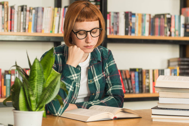 眼鏡の若い赤毛の女性図書館で本を読む - 写真・画像