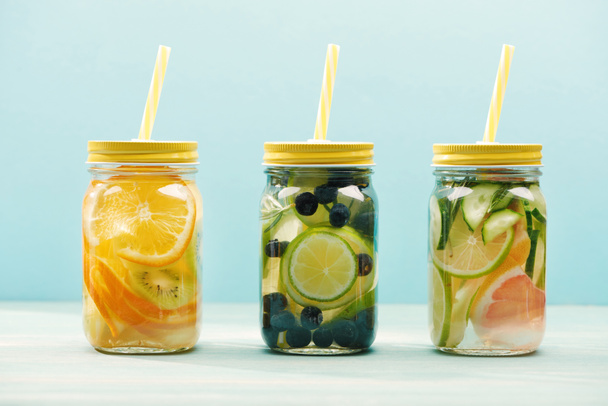 organické detoxinové nápoje s bobule, ovocem a zeleninou ve skleničkách s brzlemi izolovanými na modrém  - Fotografie, Obrázek