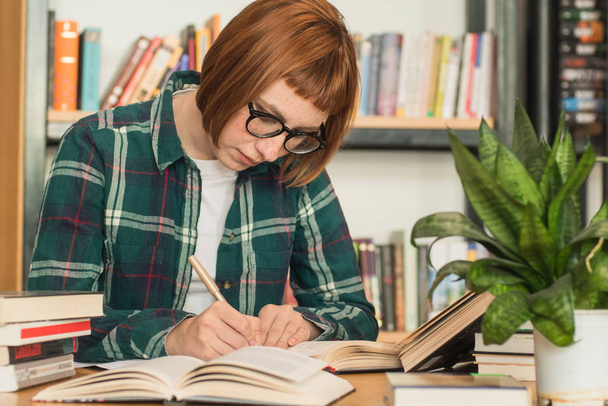 Young redhead woman in glasses read book in the library - Foto, Imagen