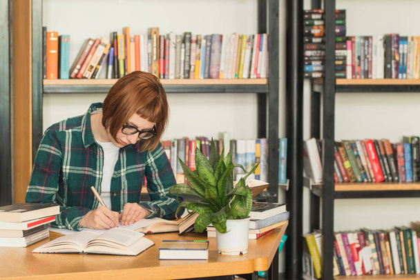 Jeune rousse femme en lunettes lire le livre dans la bibliothèque
 - Photo, image