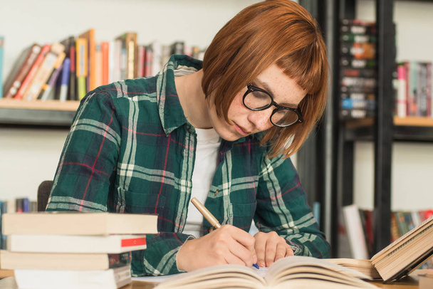 Jonge redhead vrouw in glazen leesboek in de bibliotheek - Foto, afbeelding