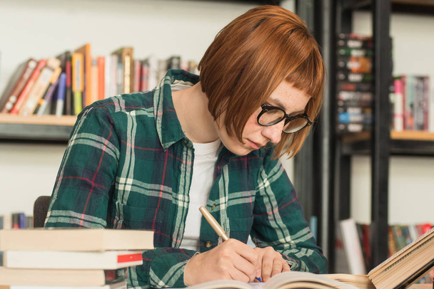 Jeune rousse femme en lunettes lire le livre dans la bibliothèque
 - Photo, image