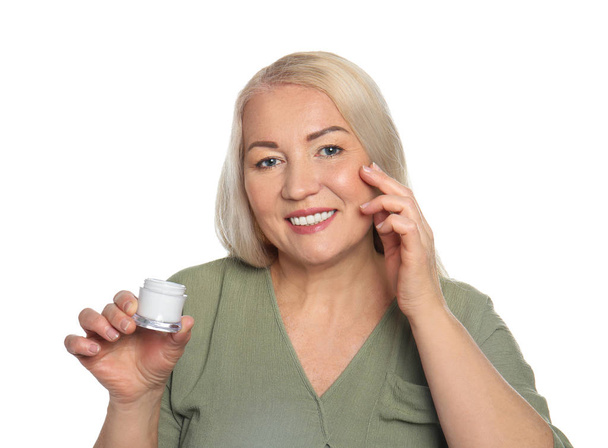 Mature woman applying facial cream on white background - Foto, afbeelding