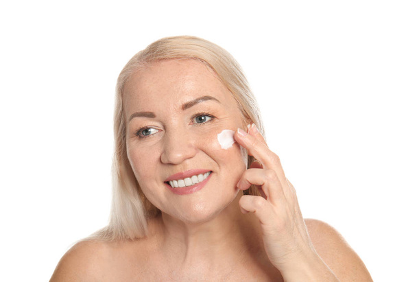 Rijpe vrouw toe te passen gezichtscrème op witte achtergrond - Foto, afbeelding