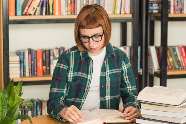 Gözlük Genç Redhead kadın kütüphanede kitap okumak - Fotoğraf, Görsel