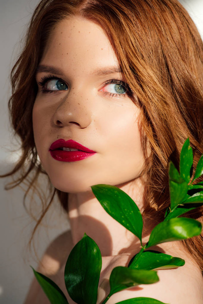 beautiful young redhead woman posing with plant and looking away - Foto, afbeelding