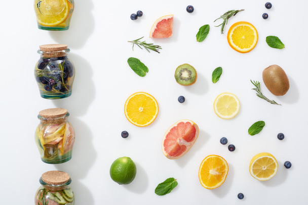 top view of detox drinks in jars near fruit slices, berries and herbs - Foto, imagen