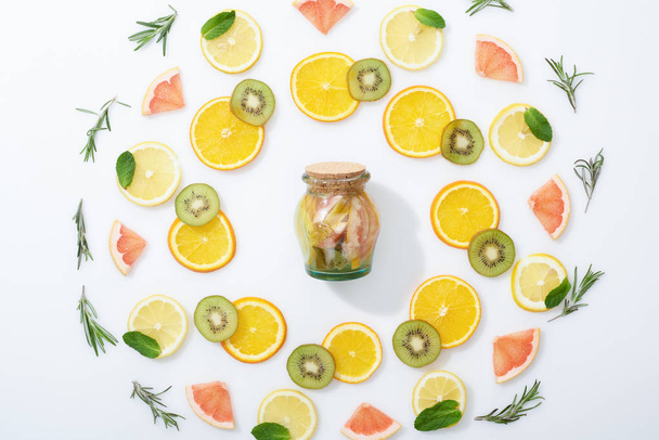 flat lay with fresh sliced kiwi, oranges, lemons, grapefruits, mint, rosemary and detox drink in jar  - Foto, immagini