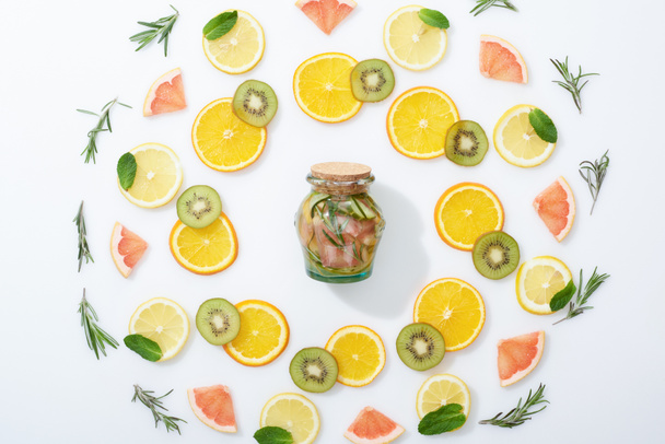 flat lay with sliced kiwi, oranges, lemons, grapefruits, mint, rosemary and fresh detox drink in jar on grey background - Photo, Image