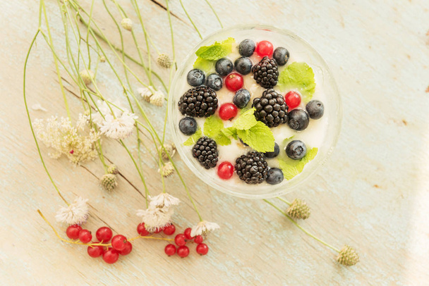Summer light breakfast. Berries with yogurtmo and simple flowers. Vintage style. - Фото, изображение