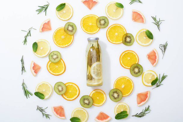 flat lay with sliced kiwi, oranges, lemons, grapefruits, mint, rosemary and detox beverage in bottle on grey background - Фото, изображение