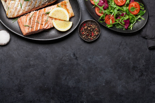 Filete de salmón a la parrilla con sal, pimienta y romero. servido con hojas de ensalada sobre fondo de piedra
 - Foto, imagen