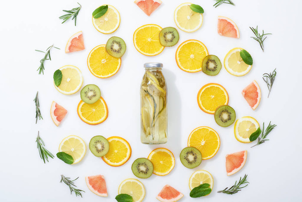 flat lay with sliced kiwi, oranges, lemons, grapefruits, mint, rosemary and detox drink in bottle on grey background - Fotó, kép