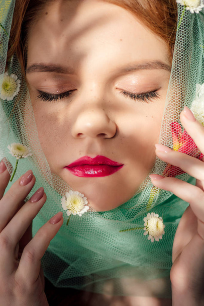 szép fiatal nő szeme zárva, és piros ajkak borított fátylat virágokkal - Fotó, kép