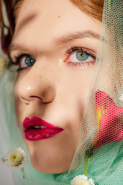 beautiful young woman with red lips covered in veil with flowers looking away - Фото, зображення