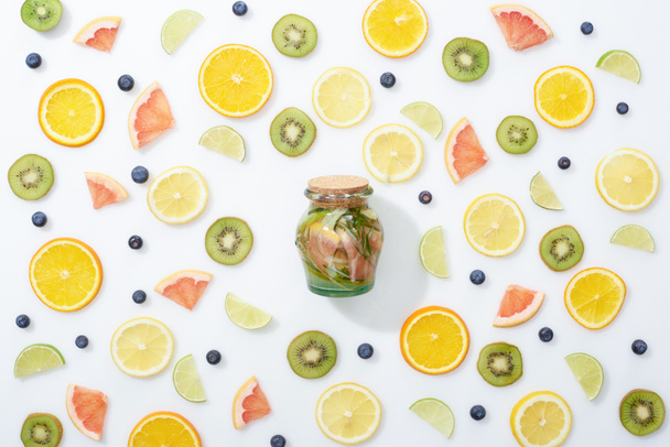 bovenaanzicht van detox drink in jar onder gesneden fruit en bosbessen op witte achtergrond - Foto, afbeelding