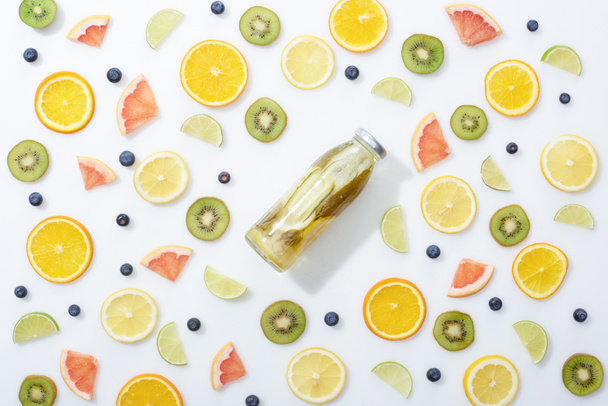 Beyaz arka planda dilimlenmiş meyve ve yaban mersini arasında şişe detoks içecek üst görünümü - Fotoğraf, Görsel