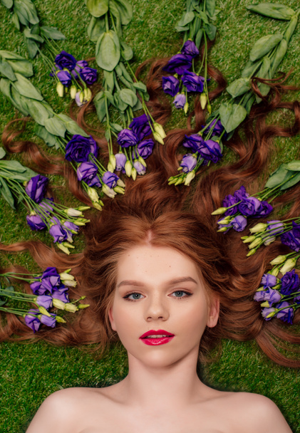 top view of beautiful young redhead woman with red lips and eustoma flowers in hair  - Zdjęcie, obraz
