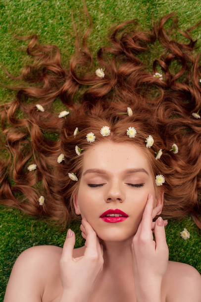 beautiful young redhead woman with red lips and chrysanthemum flowers in hair touching face - Foto, imagen