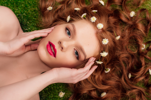 beautiful young redhead woman with red lips and chrysanthemum flowers in hair touching face - Fotó, kép