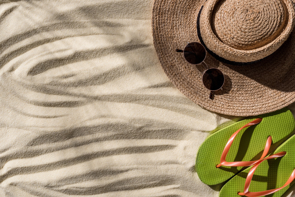 vista superior de sombrero de paja, chanclas y gafas de sol en arena ondulada con espacio para copiar
 - Foto, Imagen