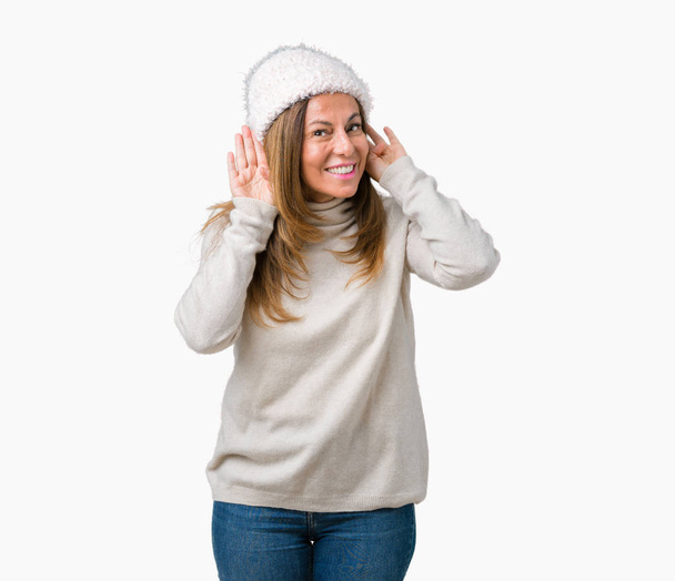 Kobieta piękna średnim wieku sobie sweter zimowy i kapelusz na białym tle stara się usłyszeć obie ręce na ucho gest, ciekawy dla plotek. Problem słuchu, głuchy - Zdjęcie, obraz