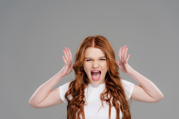 beautiful redhead girl looking at camera, gesturing with hands and yelling isolated on grey - Фото, изображение