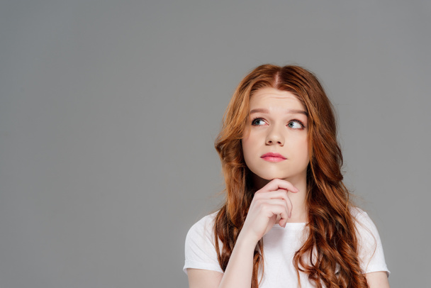 thoughtful redhead girl propping chin with hand isolated on grey with copy space - Zdjęcie, obraz