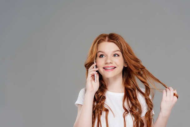 beautiful redhead girl talking on smartphone and smiling isolated on grey with copy space - Фото, изображение