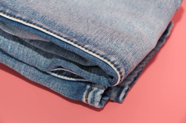 Folded blue jeans on a pink background. Faded blue jeans. - Photo, Image