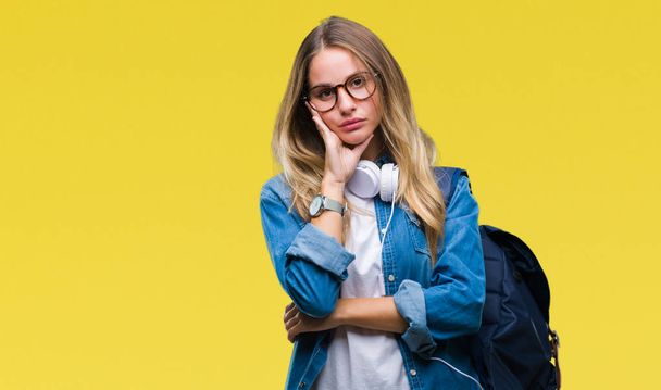 Fiatal gyönyörű szőke diák nő visel a fejhallgató és a szemüveg alatt elszigetelt háttér gondolkodás látszó fáradt, és unatkozni a depresszió problémák karokkal. - Fotó, kép