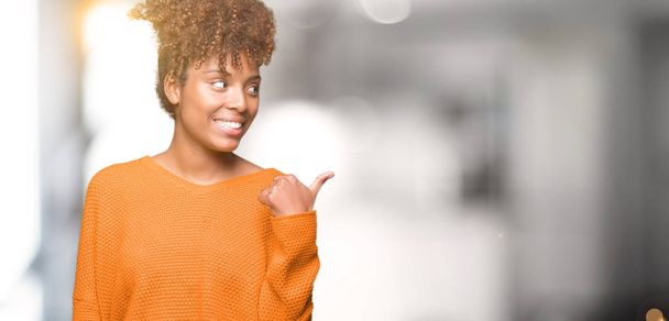 Красивая молодая африканская американка на изолированном фоне улыбается со счастливым лицом, глядя и указывая на сторону с большим пальцем вверх
. - Фото, изображение
