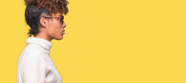 Beautiful young african american woman wearing glasses over isolated background looking to side, relax profile pose with natural face with confident smile. - Photo, Image